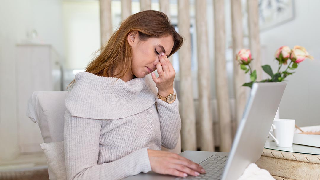 Woman sitting in front of laptop pinching the bridge of her nose in despair